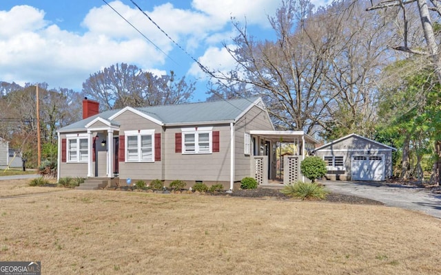 view of front facade featuring aphalt driveway, an outbuilding, a chimney, a garage, and a front lawn