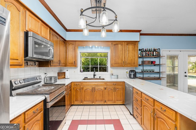 kitchen featuring tile countertops, ornamental molding, decorative light fixtures, stainless steel appliances, and a sink