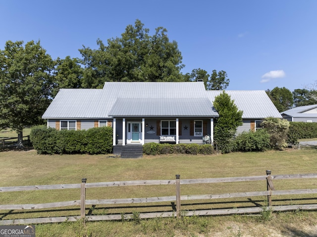 ranch-style home featuring covered porch, metal roof, fence, and a front lawn