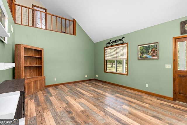 unfurnished living room with high vaulted ceiling, baseboards, and wood finished floors