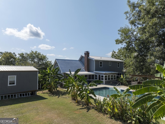 back of house with metal roof, a yard, a chimney, and an outdoor pool