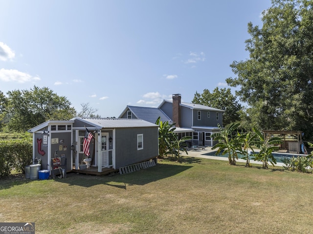 back of house with an outdoor structure, metal roof, a lawn, and a swimming pool