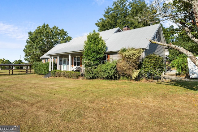 view of front of property with a chimney, metal roof, fence, a porch, and a front yard