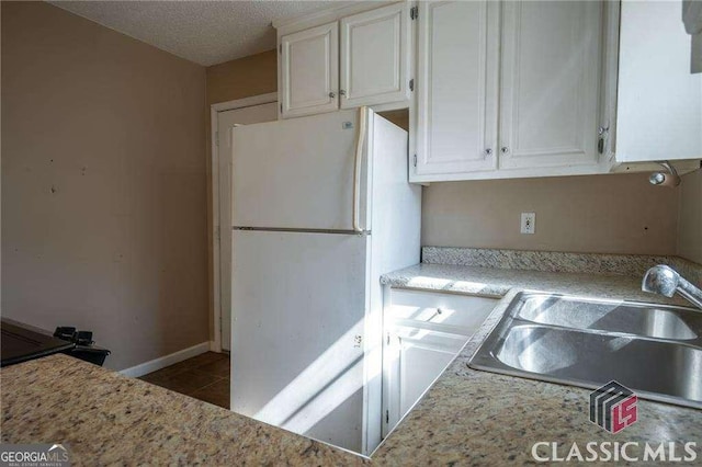 kitchen with tile patterned flooring, a sink, white cabinetry, baseboards, and freestanding refrigerator