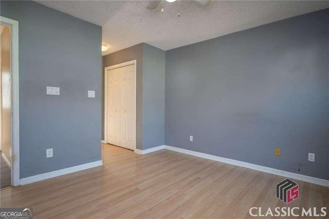 interior space featuring light wood-style floors, ceiling fan, a textured ceiling, and baseboards