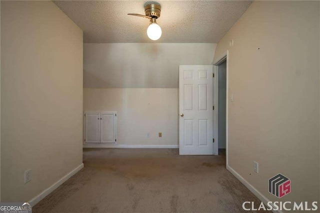 additional living space featuring light carpet, a textured ceiling, and baseboards