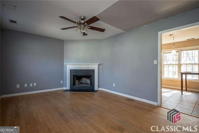 unfurnished living room featuring a ceiling fan, a fireplace with flush hearth, visible vents, and wood finished floors