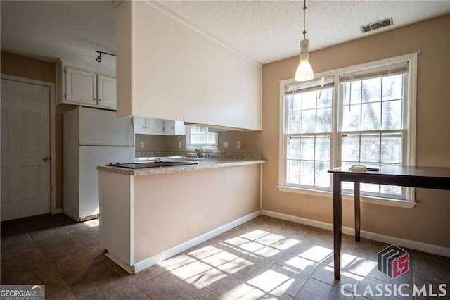 kitchen with light countertops, visible vents, hanging light fixtures, freestanding refrigerator, and a peninsula