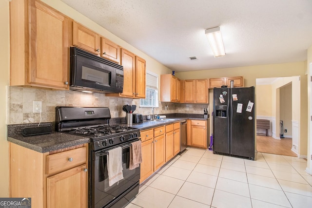 kitchen with light tile patterned floors, visible vents, dark countertops, black appliances, and a sink