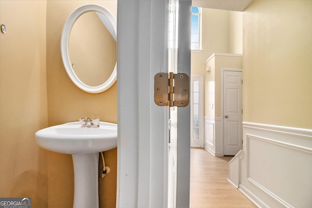 bathroom with a sink, a decorative wall, wood finished floors, and wainscoting