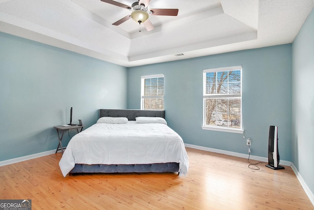 bedroom with light wood-type flooring, a raised ceiling, and baseboards