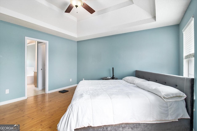 bedroom with baseboards, a tray ceiling, wood finished floors, and ensuite bathroom