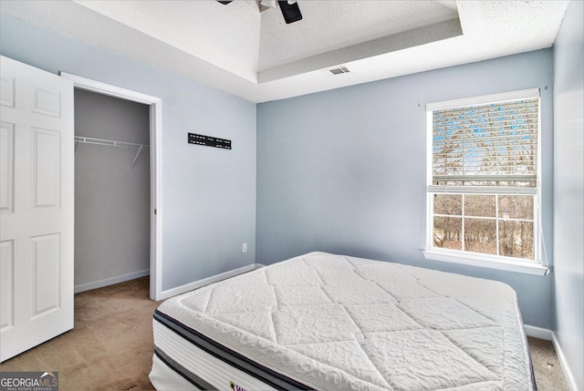 bedroom featuring light carpet, baseboards, a raised ceiling, a textured ceiling, and a closet