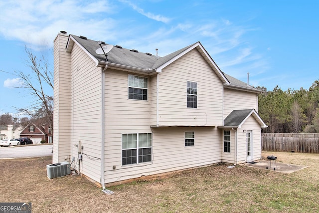 rear view of house with a patio, central air condition unit, fence, a lawn, and a chimney