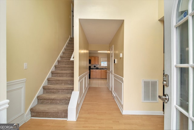 foyer entrance featuring stairway, visible vents, a decorative wall, and light wood-style flooring