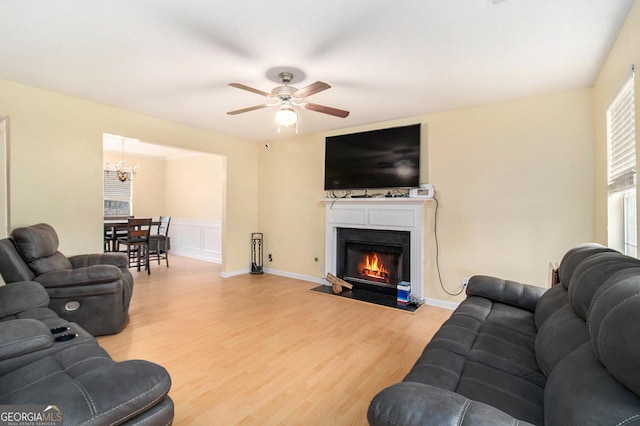 living area featuring a fireplace with flush hearth, ceiling fan, wood finished floors, and wainscoting