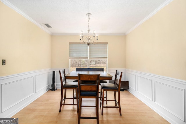 dining area with a textured ceiling, a decorative wall, visible vents, light wood finished floors, and an inviting chandelier