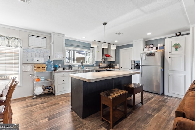 kitchen with appliances with stainless steel finishes, dark wood-style flooring, a center island, hanging light fixtures, and light countertops