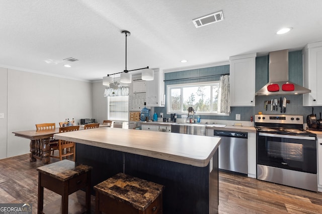 kitchen featuring a center island, light countertops, visible vents, appliances with stainless steel finishes, and wall chimney exhaust hood