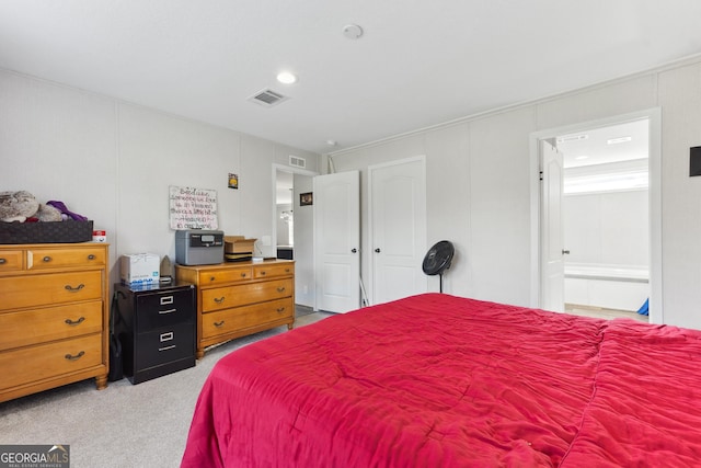 bedroom featuring a decorative wall, connected bathroom, visible vents, and light colored carpet