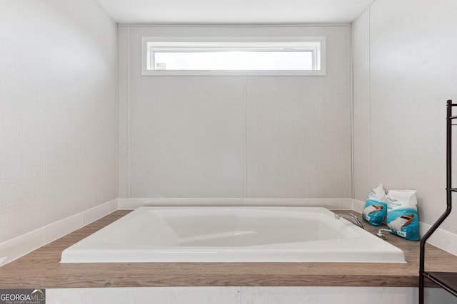 bathroom with a healthy amount of sunlight, a tub, and baseboards