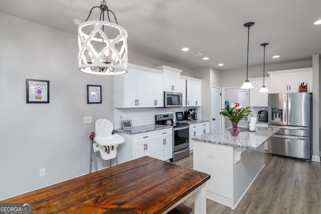 kitchen with light stone countertops, white cabinets, hanging light fixtures, appliances with stainless steel finishes, and a center island