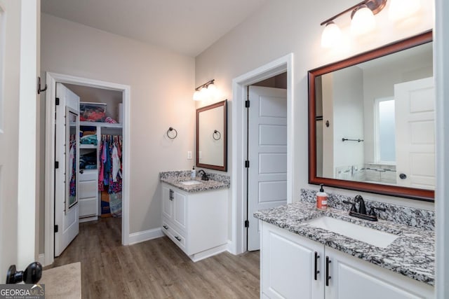 full bathroom featuring two vanities, a sink, a spacious closet, and wood finished floors