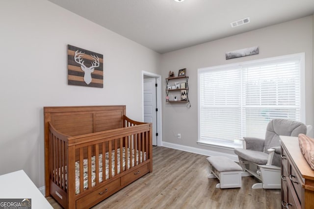 bedroom with baseboards, visible vents, light wood finished floors, and a crib