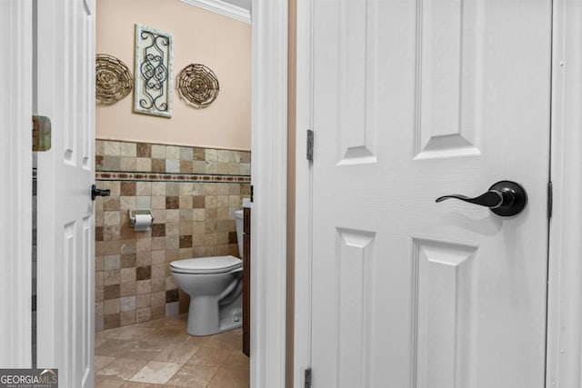 half bathroom with wainscoting, toilet, and tile walls