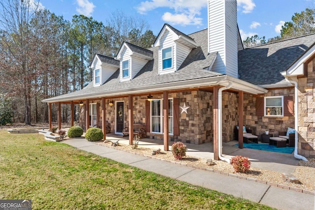 view of front facade with stone siding, a front yard, a porch, and roof with shingles