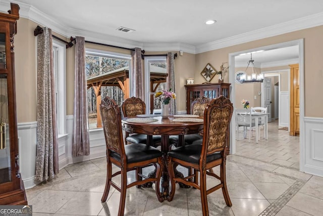 dining room featuring crown molding, visible vents, a decorative wall, wainscoting, and a chandelier