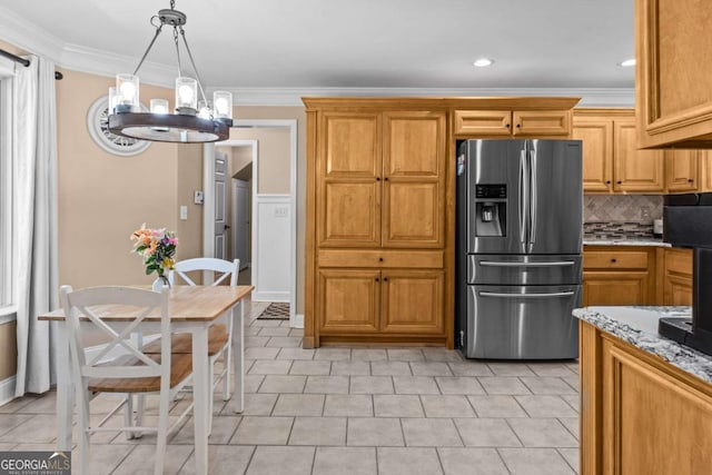 kitchen with light stone counters, stainless steel fridge, hanging light fixtures, and ornamental molding