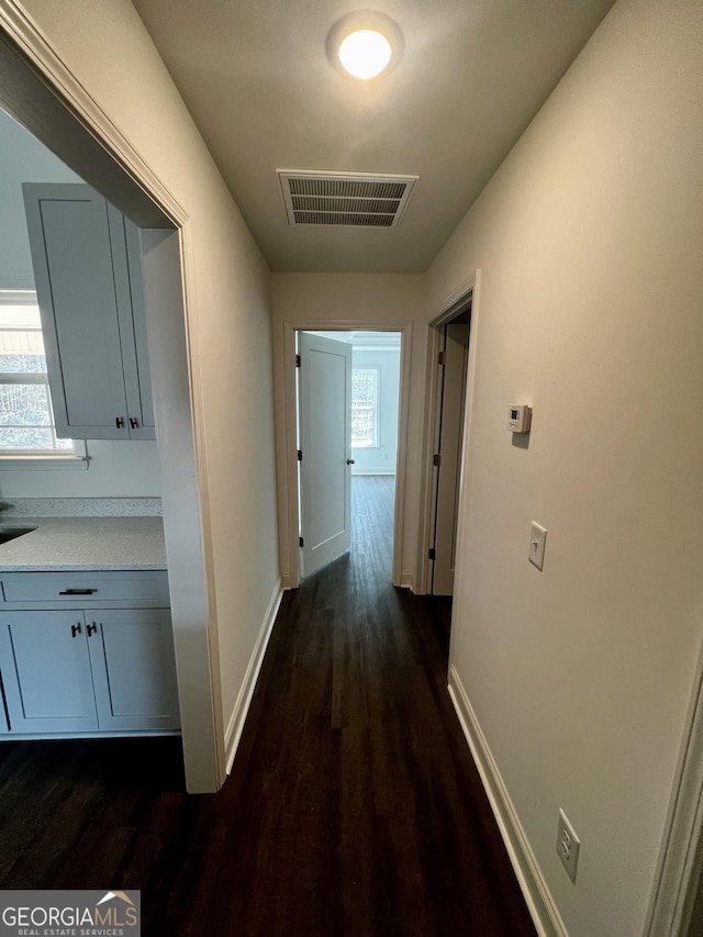 hallway featuring dark wood-style floors, baseboards, and visible vents