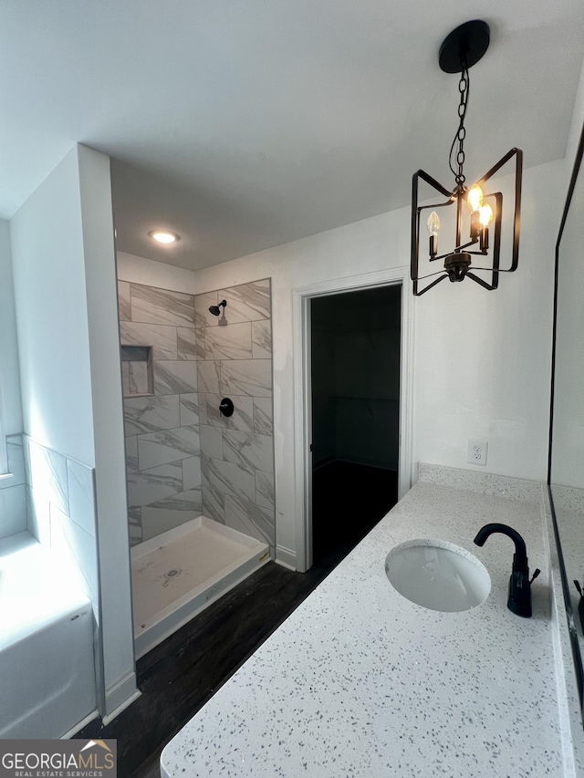 bathroom featuring a chandelier, a garden tub, wood finished floors, vanity, and a shower stall