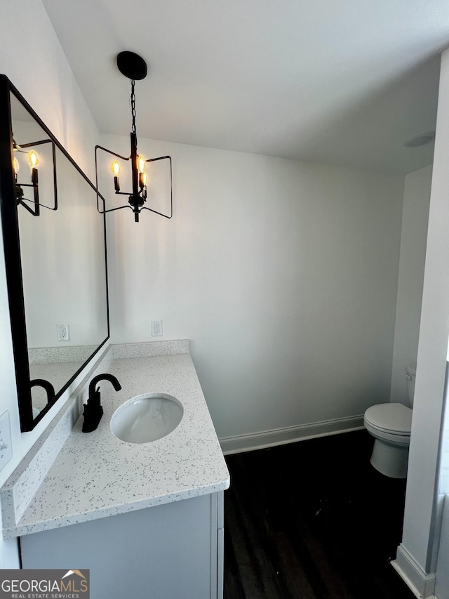 bathroom featuring a notable chandelier, toilet, vanity, wood finished floors, and baseboards