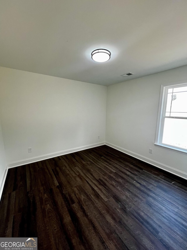 unfurnished room with baseboards, visible vents, and dark wood-style flooring