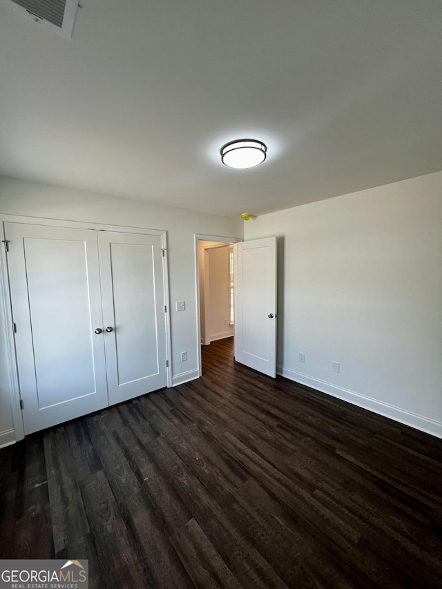 unfurnished bedroom with a closet, dark wood finished floors, visible vents, and baseboards