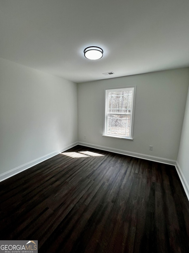 spare room featuring visible vents, baseboards, and dark wood finished floors