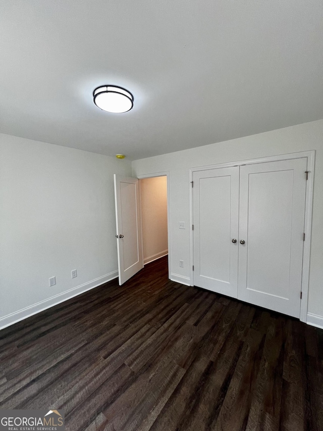 unfurnished bedroom featuring a closet, dark wood-style flooring, and baseboards