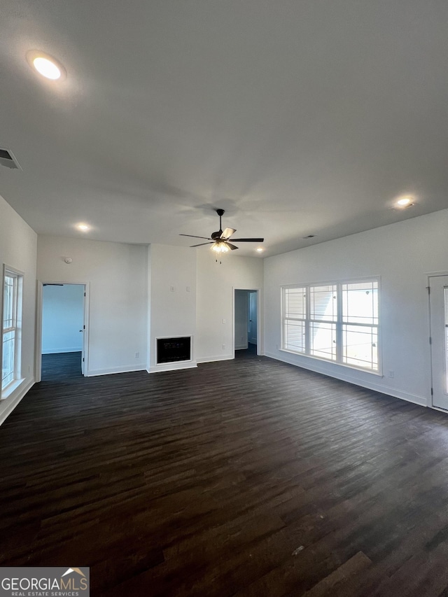 unfurnished living room featuring dark wood-type flooring, a fireplace, visible vents, a ceiling fan, and baseboards