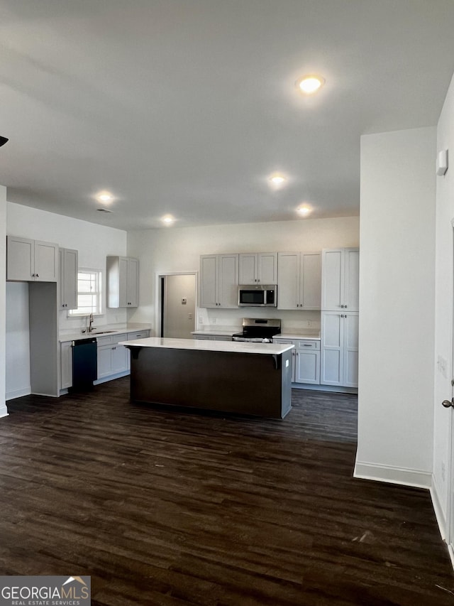 kitchen featuring dark wood-style flooring, stainless steel appliances, light countertops, a kitchen island, and a sink