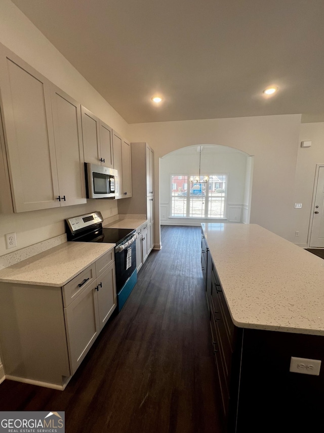 kitchen featuring dark wood-style floors, stainless steel appliances, light stone counters, and a chandelier