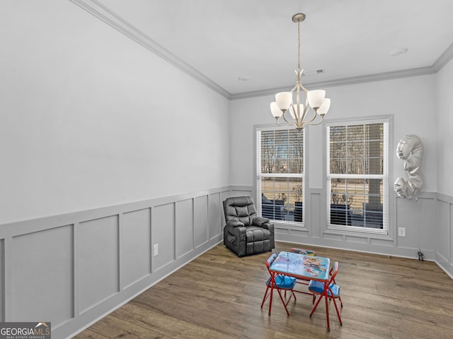 sitting room featuring a chandelier, a decorative wall, wood finished floors, and ornamental molding