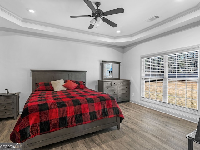 bedroom featuring visible vents, ornamental molding, a raised ceiling, and wood finished floors