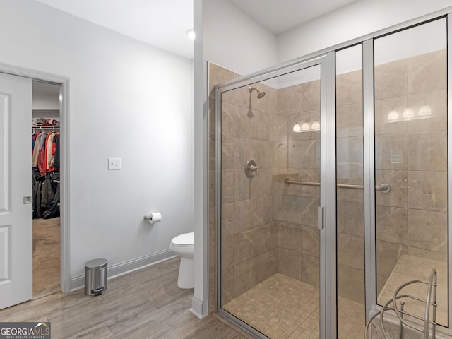 full bath with a spacious closet, toilet, a shower stall, wood finished floors, and baseboards