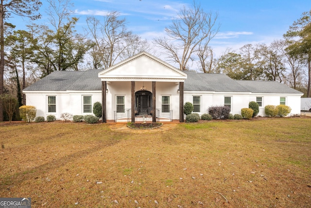 greek revival house with covered porch, a shingled roof, a front lawn, and stucco siding