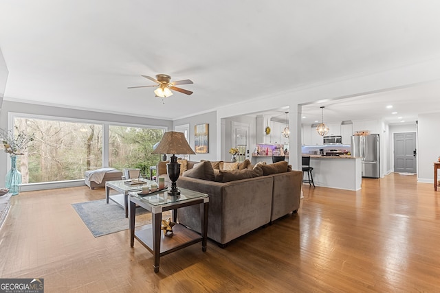 living area with light wood-style floors, recessed lighting, crown molding, and a ceiling fan