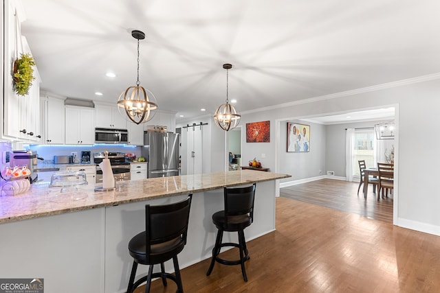 kitchen with decorative light fixtures, stainless steel appliances, a barn door, white cabinets, and a kitchen bar