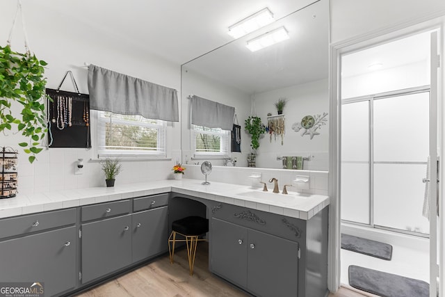 full bathroom with a shower with shower door, wood finished floors, vanity, and backsplash