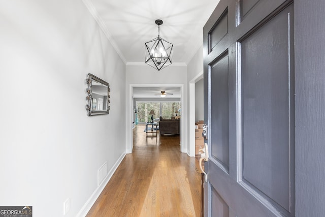 corridor with visible vents, baseboards, wood finished floors, crown molding, and a notable chandelier